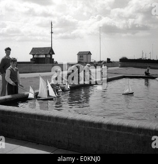 1950s historical picture of children playing with their toy sailing boats on a small man--made model lake or pond. Stock Photo