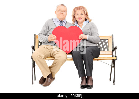Lovely mature couple holding big red heart seated on bench Stock Photo