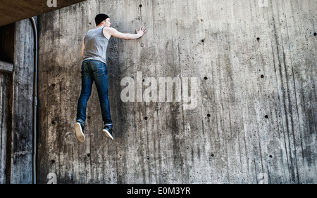 Young man jumping in a parkour move on concrete wall Urban scene with lifestyle moment of youth filled with energy and strength Stock Photo