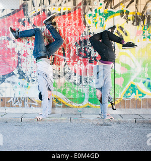 Portrait of young man and woman doing handstand in front of grafitti wall in urban area. Stock Photo