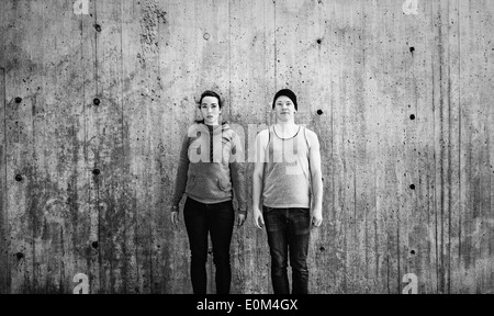 Portrait of young man and woman standing in urban area in front of concrete wall with copy space. Stock Photo