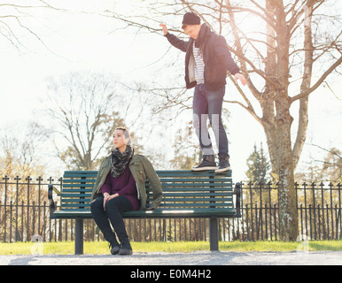 Young man trying to impress indifferent girl by balancing on a park bench. Stock Photo