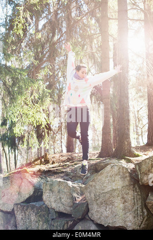 Young woman in nature jumping on the edge of big rocks in woods. Stock Photo