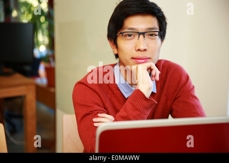 Handsome asian man sitting at the table with laptop and looking at camera Stock Photo