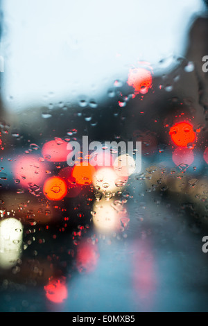 blurred light of cars seen through  a wet windshield with some raindrops on it in the early morning of a rainy day Stock Photo