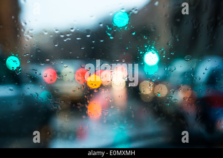 blurred light of cars seen through  a wet windshield with some raindrops on it in the early morning of a rainy day Stock Photo