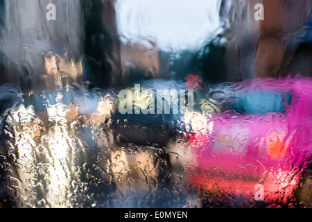 blurred light of cars seen through  a wet windshield with some raindrops on it in the early morning of a rainy day Stock Photo