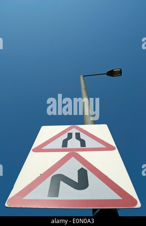 british road sign indicating a double bend, first bend to right, and a narrowing of the road ahead Stock Photo