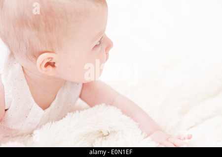 Baby girl in white dress playing on white blanket. Stock Photo