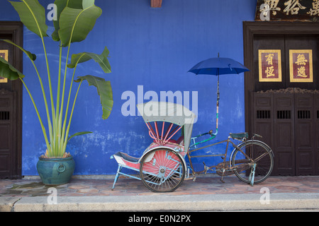 Exterior entrance shot of Cheong Fatt Tze mansion with large plant, red trishaw, and chinese calligrpahy on door. Stock Photo