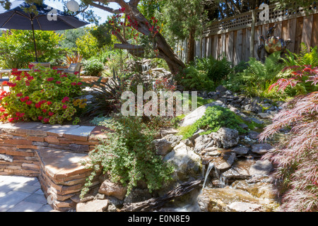Water feature stream with lush foliage in a beautiful landscaped backyard with stacked flagstone wall Stock Photo