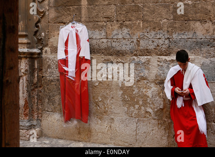 A penitent checks his mobile phone before the start  of an easter Sunday palm procession in the island of Majorca, Spain Stock Photo