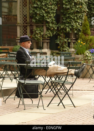 Old man sitting at a table outside with feet up Stock Photo