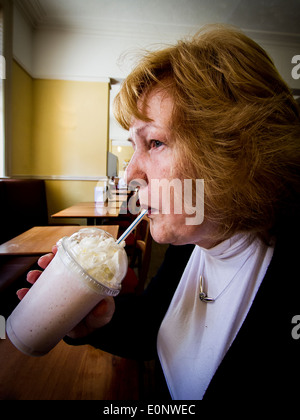 Lady in a restaurant drinking a milkshake with cream topping through a straw Stock Photo