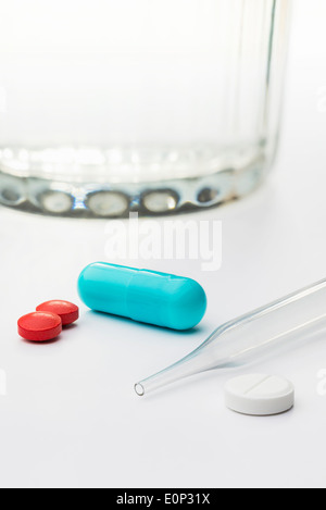 Colored capsiles and pills, with a glass of water and a dropper Stock Photo