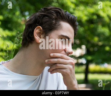 Unhappy, sad young man outdoors in park thinking, profile view Stock Photo