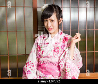 Asian woman in kimono standing by wooden framed windows Stock Photo