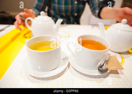 Closeup of two cups of herbal tea with tea pots and woman sitting in background Stock Photo