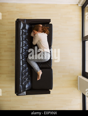 Overhead view of young woman sleeping on sofa by a door. Aerial view of caucasian female relaxing on couch at home. Stock Photo