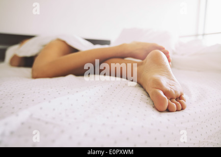 Young female sleeping in bed at home with focus on legs. Feet of woman lying on bed. Stock Photo