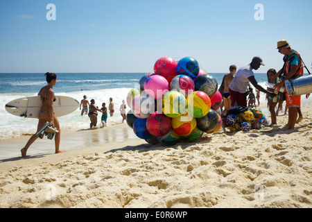 RIO DE JANEIRO, BRAZIL - JANUARY 20, 2014: Woman walks with surfboard on Ipanema Beach past vendors selling beach balls and food