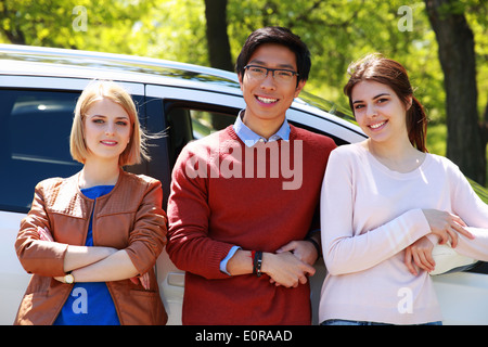 Happy young friends leaning on the car in park Stock Photo