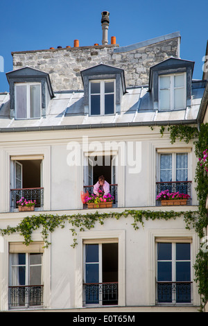 Woman trimming geraniums on the window balcony of her apartment in the Marais district of Paris France Stock Photo