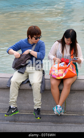 London, England, UK. Young Asian couple sitting on a fountain in Trafalgar Square Stock Photo