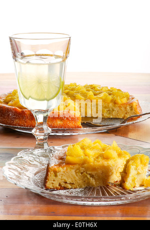 Sweet cake with rhubarb and apples on glass plate icing sugar, rough painted wooden table, lemonade in glass Stock Photo