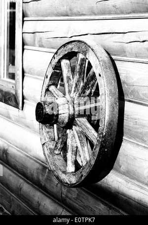 The old wooden wheel from a cart hangs on a wall from natural logs Stock Photo