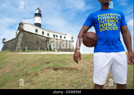 Brazilian football player standing with vintage soccer ball at the Farol da Barra lighthouse in Salvador Brazil Stock Photo