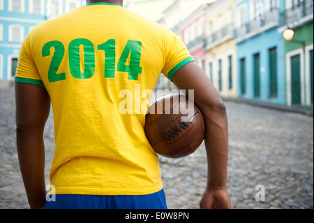 Brazilian football player in 2014 shirt standing holding soccer ball in colorful colonial plaza Pelourinho Salvador Bahia Brazil Stock Photo