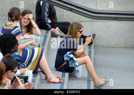 London, England, UK. People relaxing on the steps leading from Trafalgar Square to the National gallery - girl texting