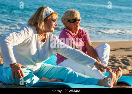 Elderly women doing stretching exercises on beach. Stock Photo