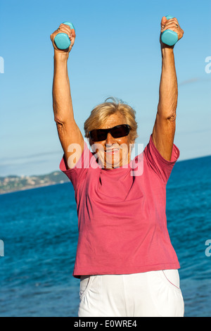 Senior woman doing muscle exercise on beach. Stock Photo