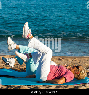 Senior women doing leg exercises on beach. Stock Photo