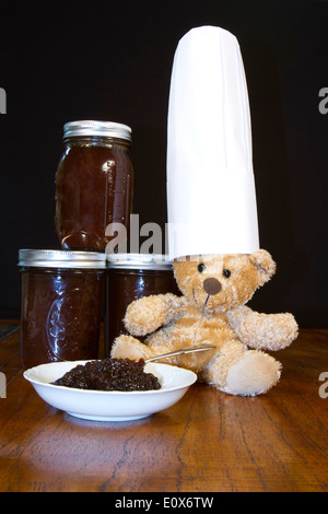 Teddy bear wearing a chef's hat with jars and bowl of apple butter jelly Stock Photo