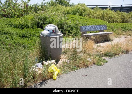 Trash and overflowing trash can and a graffiti covered bench at a roadside stop in California Stock Photo