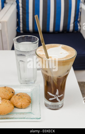 Iced coffee, a glass of water with some biscuits on a table in Greece Stock Photo