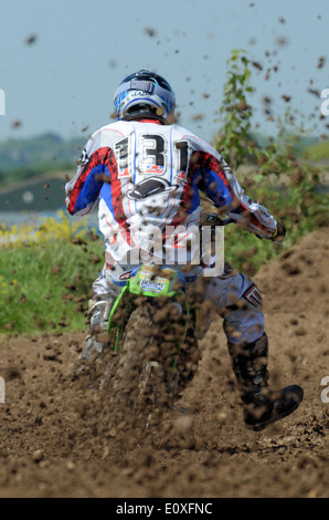 Motocross is a form of motorcycle racing held on rough enclosed off-road circuits. Motorbike rider on scramble bike, kicking up mud in rooster tail Stock Photo