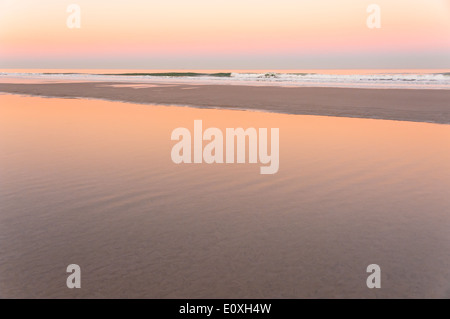 Beautiful pastel colors of dusk reflect in the thin skim of water covering the wet sand at Jacksonville Beach, Florida, USA. Stock Photo