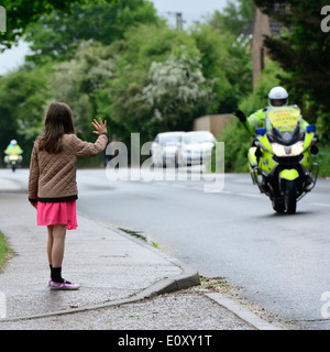 Young white girl waving at British police motorbike rider who waves back while riding past.Manningtree,Essex,UK Stock Photo