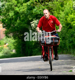 Royal Mail postman on a bicycle with a basket and side pannier carrying letters riding up a steep hill in Manningtree,Essex,UK Stock Photo