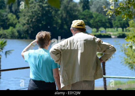 Retirees / pensioners, senior couple resting and walking by a lake in a park Stock Photo