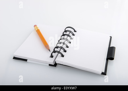 Open black and white ringed notepad and pencil resting on a white desk Stock Photo