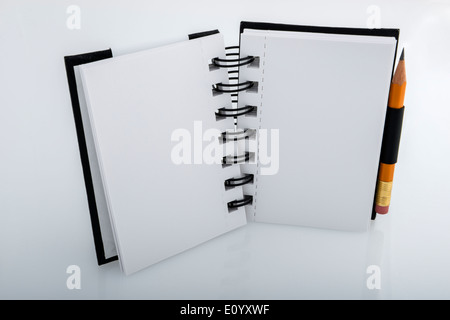 Standing open black and white ringed notepad and pencil resting on a white desk Stock Photo