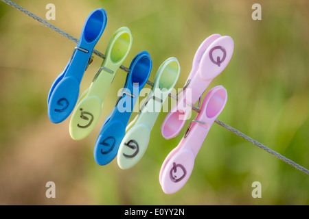 Multi colored clothing pins attached to a clothing line with a blurred green background Stock Photo