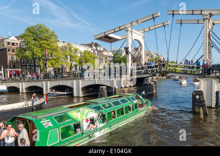 Amsterdam Heineken shuttle canal cruise boat with Magere Brug, Skinny Bridge, on the Amstel River canal with small boats Stock Photo