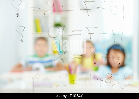 Image of sums written on transparent board with schoolmates on background Stock Photo