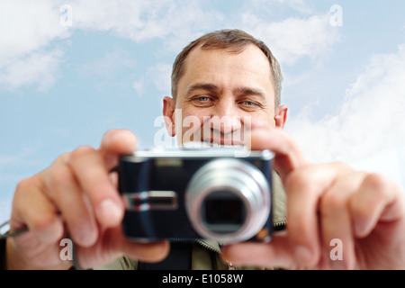 Portrait of mature man taking pictures against cloudy sky Stock Photo
